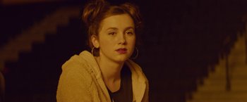 Movie still from “Assassination Nation” (2018), directed by Sam Levinson – A woman with a brown jacket and a black shirt; Close Up shot, Over the shoulder angle