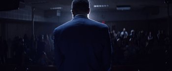 Movie still from “Assassination Nation” (2018), directed by Sam Levinson – A man in a suit standing in front of a group of people; Medium shot, Low angle