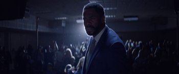Movie still from “Assassination Nation” (2018), directed by Sam Levinson – A man wearing a suit and tie standing in front of an audience; Close Up shot, Low angle