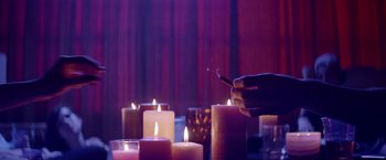 Movie still from “Assassination Nation” (2018), directed by Sam Levinson – A person lighting a cigarette in front of a group of lit candles; Medium shot, Low angle