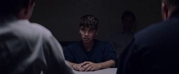 Movie still from “Assassination Nation” (2018), directed by Sam Levinson – A man sitting at a table with his hands folded on his chest; Close Up shot, Over the shoulder angle