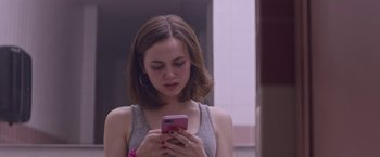 Movie still from “Assassination Nation” (2018), directed by Sam Levinson – A woman looking at her cell phone while standing in front of a mirror; Close Up shot, Over the shoulder angle