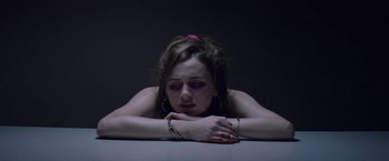Movie still from “Assassination Nation” (2018), directed by Sam Levinson – A woman sitting at a table with her head resting on her hands; Close Up shot, Overhead angle