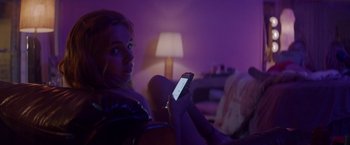 Movie still from “Assassination Nation” (2018), directed by Sam Levinson – A woman sitting in a chair looking at her phone; Medium shot, Low angle