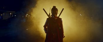 Movie still from “Assassination Nation” (2018), directed by Sam Levinson – A person in a samurai outfit holding two swords; Medium shot, Low angle