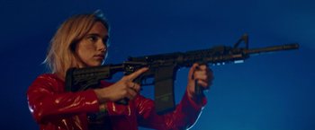 Movie still from “Assassination Nation” (2018), directed by Sam Levinson – A woman in a red jacket holding a gun; Medium shot, Low angle