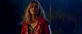 Movie still from “Assassination Nation” (2018), directed by Sam Levinson – A woman in a red leather jacket standing in a darkened room; Close Up shot, Over the shoulder angle