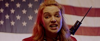 Movie still from “Assassination Nation” (2018), directed by Sam Levinson – A person making a funny face in front of an american flag; Close Up shot, Low angle