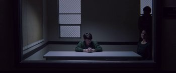 Movie still from “Assassination Nation” (2018), directed by Sam Levinson – A man sitting at a table in a dark room; Wide shot, High angle