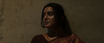 A woman in a sari is standing against a wall