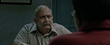 An older man with a mustache sitting in front of another man