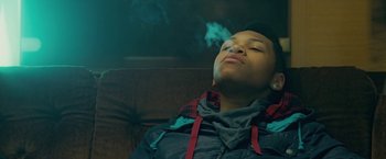 Movie still from “Attack the Block” (2011), directed by Joe Cornish – A man is smoking a cigarette while sitting on a couch; Medium shot, Low angle