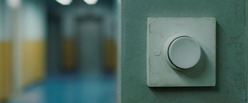 Movie still from “Attack the Block” (2011), directed by Joe Cornish – A white button on the wall in a room; Extreme Close Up shot, Overhead angle