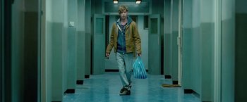 Movie still from “Attack the Block” (2011), directed by Joe Cornish – A man walking down a hallway holding a bag; Medium shot, Low angle