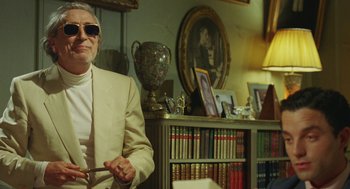 Movie still from “Attila Marcel” (2013), directed by Sylvain Chomet – An older man in a white suit holding a pair of scissors; Medium shot, Over the shoulder angle