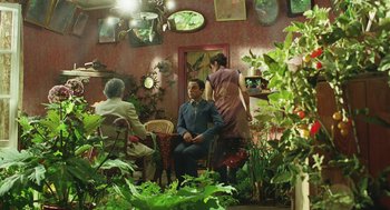 Movie still from “Attila Marcel” (2013), directed by Sylvain Chomet – A man sitting on a chair in a room with people; Wide shot, Over the shoulder angle