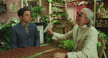 Movie still from “Attila Marcel” (2013), directed by Sylvain Chomet – Two men sitting at a table with plants in front of them; Medium shot, Over the shoulder angle