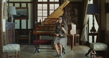 Movie still from “Attila Marcel” (2013), directed by Sylvain Chomet – A woman sitting in front of a piano holding a cello; Wide shot, High angle