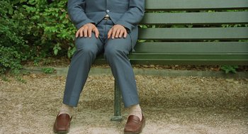 Movie still from “Attila Marcel” (2013), directed by Sylvain Chomet – A man sitting on top of a wooden bench wearing a suit; Wide shot, High angle