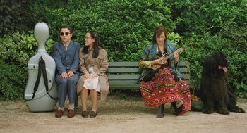 Movie still from “Attila Marcel” (2013), directed by Sylvain Chomet – Three people sitting on a park bench with a woman playing an instrument; Wide shot, High angle