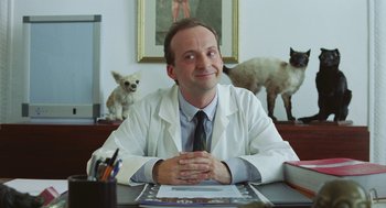 Movie still from “Attila Marcel” (2013), directed by Sylvain Chomet – A man sitting at a desk with a dog and cat in the background; Medium shot, Low angle