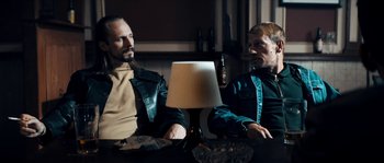 Movie still from “Avengement” (2019), directed by Jesse V. Johnson – A couple of men sitting at a table with a lamp; Medium shot, Low angle