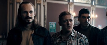 Movie still from “Avengement” (2019), directed by Jesse V. Johnson – Two men standing next to each other in front of a wall; Medium shot, Low angle