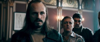 Movie still from “Avengement” (2019), directed by Jesse V. Johnson – A man with long hair is standing next to another man; Close Up shot, Low angle