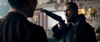 Movie still from “Avengement” (2019), directed by Jesse V. Johnson – A man holding a gun pointed at another man in front of a fireplace; Close Up shot, Over the shoulder angle