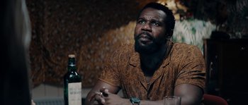 Movie still from “Avengement” (2019), directed by Jesse V. Johnson – A man sitting at a table with a bottle of wine; Close Up shot, Over the shoulder angle