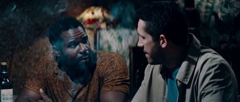 Movie still from “Avengement” (2019), directed by Jesse V. Johnson – Two men are sitting in a room and one of them is smoking a cigarette; Close Up shot, Over the shoulder angle