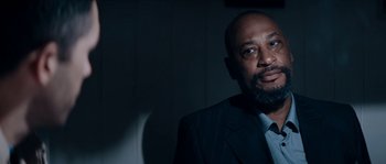 Movie still from “Avengement” (2019), directed by Jesse V. Johnson – A man wearing a suit and tie in a dark room; Close Up shot, Low angle