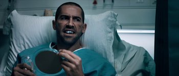 Movie still from “Avengement” (2019), directed by Jesse V. Johnson – A man in a hospital bed holding a cell phone; Close Up shot, Over the shoulder angle