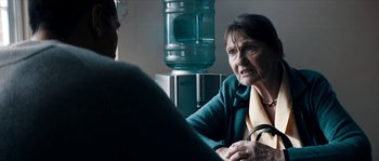 Movie still from “Avengement” (2019), directed by Jesse V. Johnson – An older woman sitting in front of a water cooler; Close Up shot, Over the shoulder angle