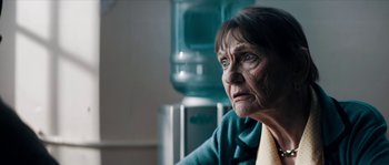 Movie still from “Avengement” (2019), directed by Jesse V. Johnson – An older woman sitting in front of a water cooler; Close Up shot, Over the shoulder angle