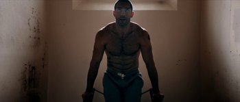 Movie still from “Avengement” (2019), directed by Jesse V. Johnson – A shirtless man holding a jump rope in a room; Medium shot, Overhead angle