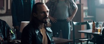 Movie still from “Avengement” (2019), directed by Jesse V. Johnson – A man with long hair and a beard sitting at a table; Close Up shot, Over the shoulder angle