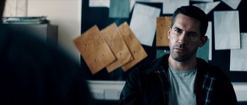 Movie still from “Avengement” (2019), directed by Jesse V. Johnson – A man sitting in front of a bulletin board; Medium shot, Over the shoulder angle