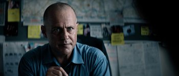 Movie still from “Avengement” (2019), directed by Jesse V. Johnson – A man in a blue shirt is sitting at a desk; Close Up shot, Over the shoulder angle