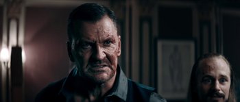 Movie still from “Avengement” (2019), directed by Jesse V. Johnson – An older man with a bruised face stares at the camera; Close Up shot, Low angle