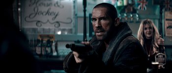 Movie still from “Avengement” (2019), directed by Jesse V. Johnson – A person holding a gun in a room; Close Up shot, Over the shoulder angle