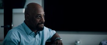 Movie still from “Avengement” (2019), directed by Jesse V. Johnson – A man sitting in front of a tv in a room; Close Up shot, Low angle