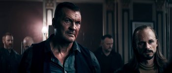 Movie still from “Avengement” (2019), directed by Jesse V. Johnson – A man with a black shirt is looking at the camera; Close Up shot, Low angle