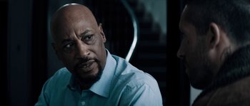 Movie still from “Avengement” (2019), directed by Jesse V. Johnson – A man with a beard is sitting in front of a staircase; Close Up shot, Over the shoulder angle