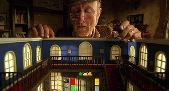Movie still from “Babe” (1995), directed by Chris Noonan – An older man holding a toy house in a room; Medium shot, Low angle