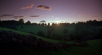 Movie still from “Babe” (1995), directed by Chris Noonan – The sun is setting over a lush green field; Extreme Wide shot, Low angle
