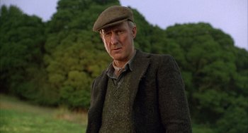 Movie still from “Babe” (1995), directed by Chris Noonan – A man wearing a hat and a jacket standing in front of trees; Close Up shot, Low angle