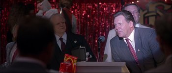 Movie still from “Backdraft” (1991), directed by Ron Howard – Two men are sitting at a podium in front of microphones; Medium shot, Over the shoulder angle