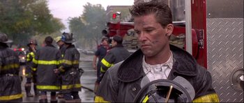 Movie still from “Backdraft” (1991), directed by Ron Howard – A man in a fireman's uniform is standing in front of a group of firemen; Close Up shot, Over the shoulder angle