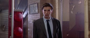 Movie still from “Backdraft” (1991), directed by Ron Howard – A man in a suit and tie standing in front of a brick wall; Medium shot, Low angle